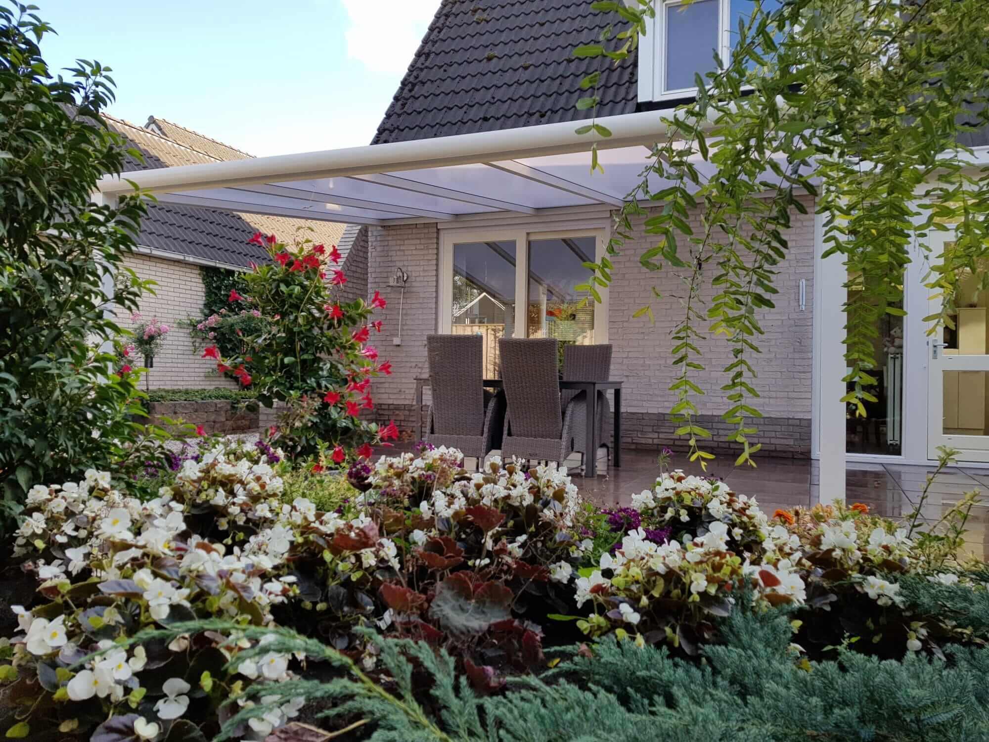 Terrassenüberdachung nach Maß in elegantem Design, umgeben von farbenfrohen Blumen und Gartenpflanzen
