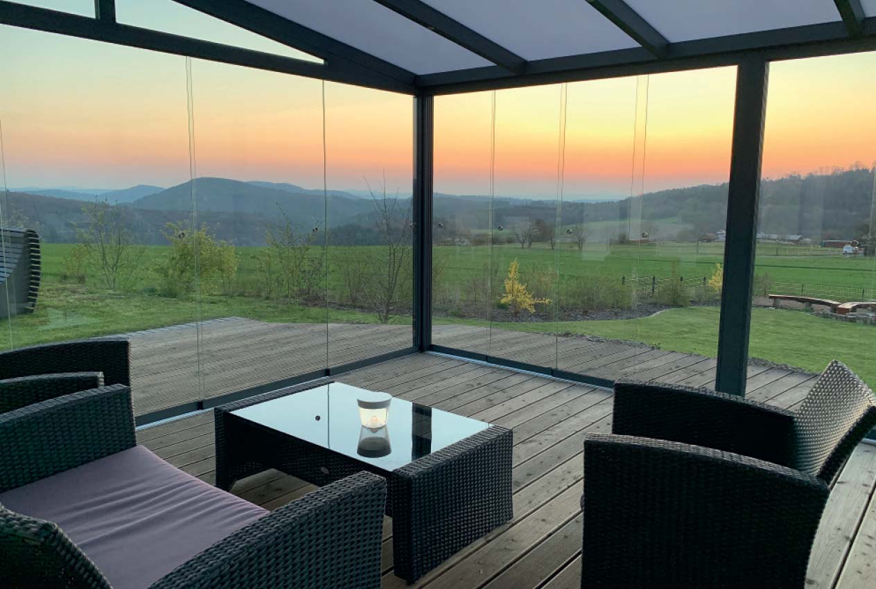  Wintergarten mit Glasschiebewänden und freiem Blick auf die Natur bei Sonnenuntergang.